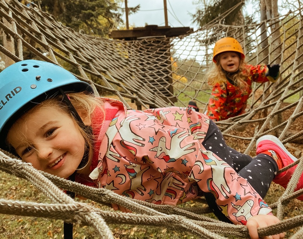 Two young girls wearing helmets and waterproofs on a rope net